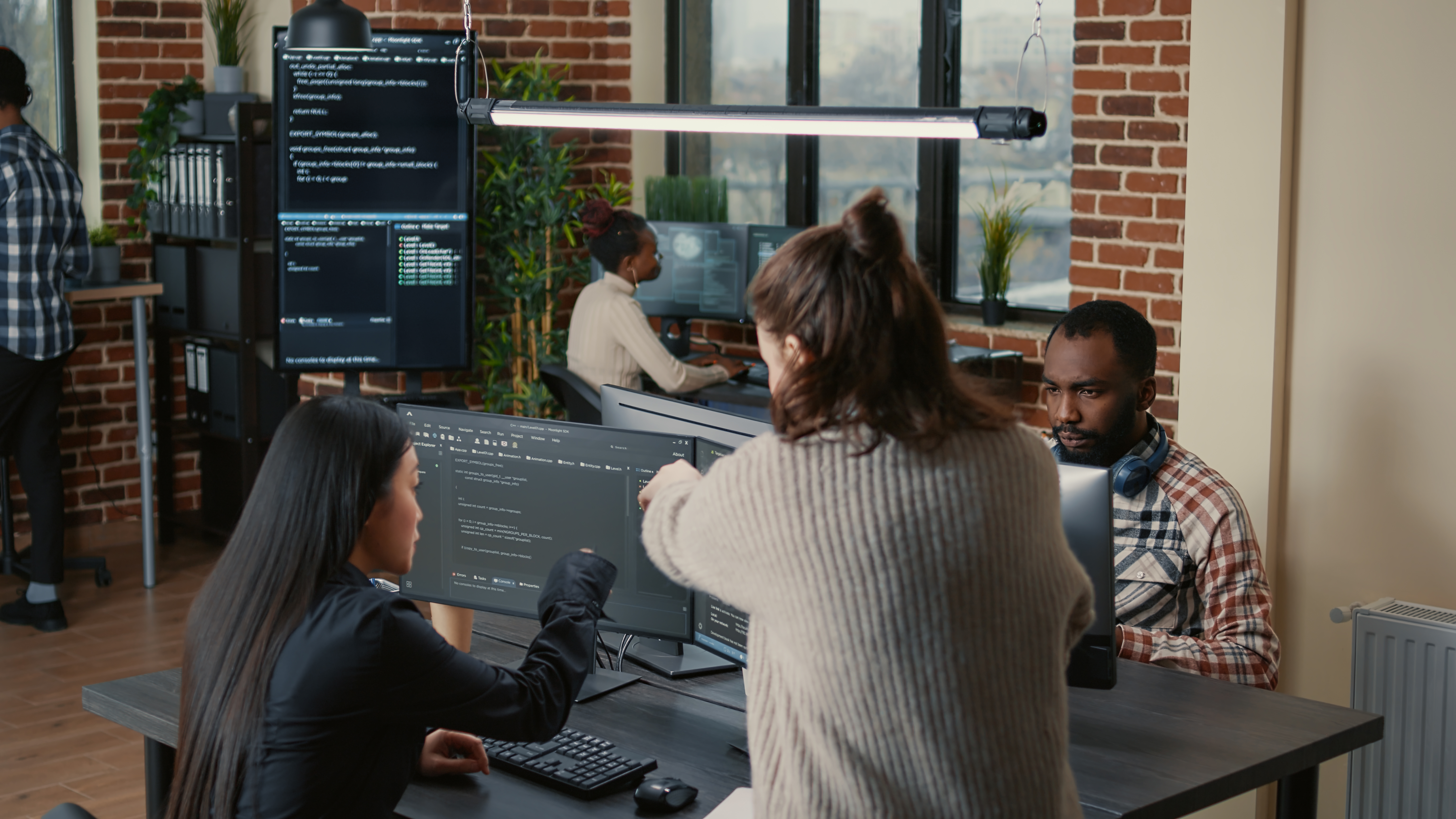 Software programer pointing pencil at source code on computer screen explaining algorithm to coworker standing next to desk. Programmers discussing online cloud computing with team.